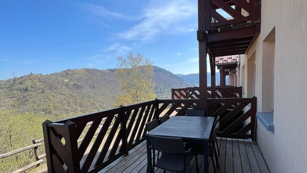 Eine Holzdiele mit Tisch und Stühlen, mit Blick auf eine gebirgige Landschaft.