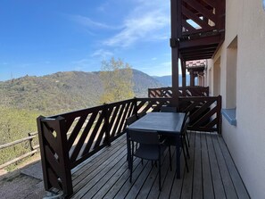 Una terraza de madera con una mesa y sillas, con vista a un paisaje montañoso.
