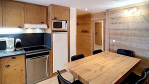 Una cocina compacta con armarios de madera, un microondas, un refrigerador, un lavavajillas y una mesa de comedor con sillas.