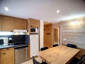 A compact kitchen with wooden cabinets, a microwave, a refrigerator, a dishwasher, and a dining table with chairs. - Spacious 3-room cabin, 6 pers, ski-in/ski-out, free parking (Les Belleville)