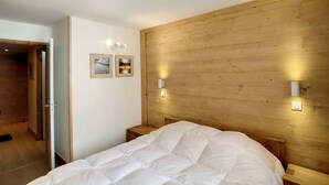 A bedroom with a wooden headboard, a bed with white bedding, two wall-mounted lights, and two framed pictures on the wall. - Spacious 3-room cabin, 6 pers, ski-in/ski-out, free parking (Les Belleville)