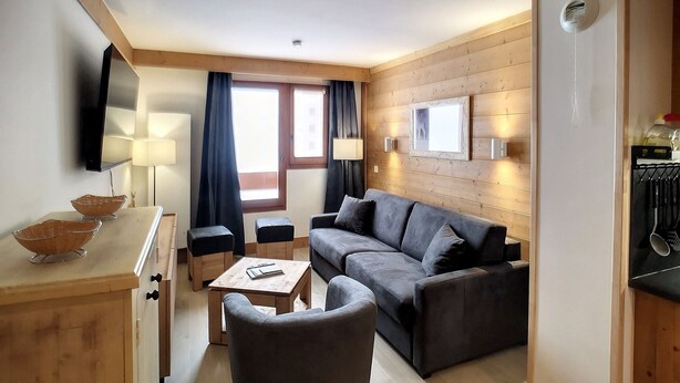 Una sala de estar moderna con un sofá, una mesita, un televisor y una ventana con cortinas.
