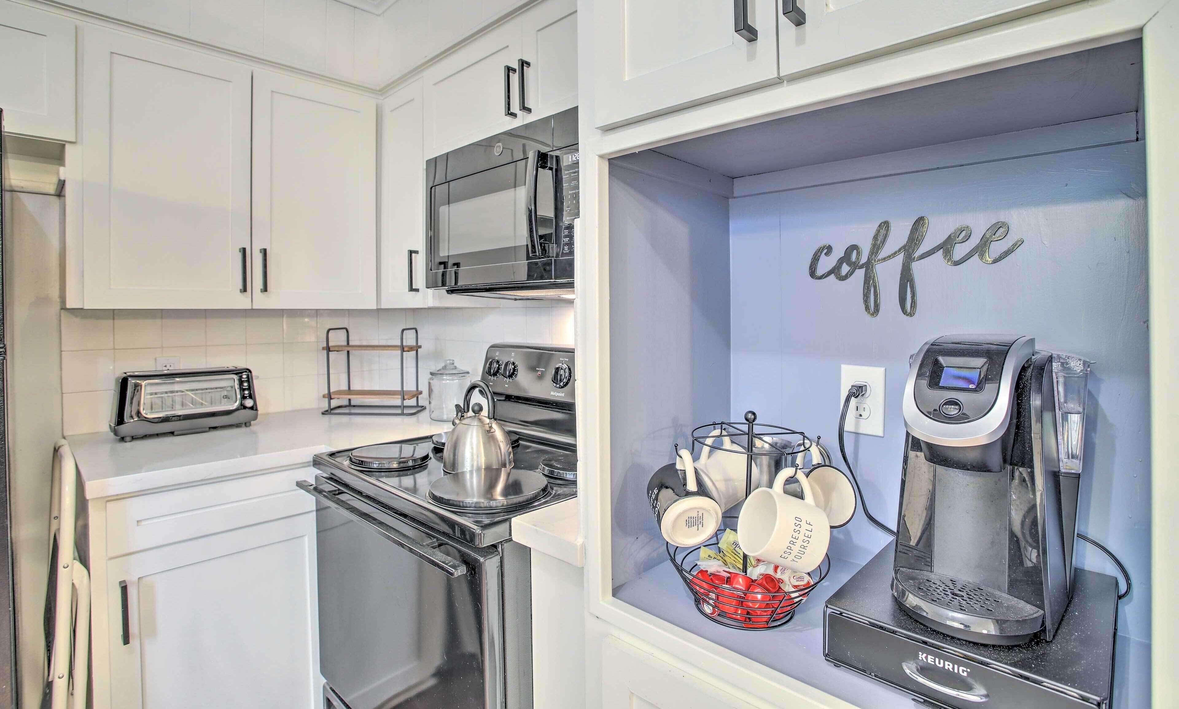 A kitchen with white cabinets, a stove, a microwave, and a coffee machine.