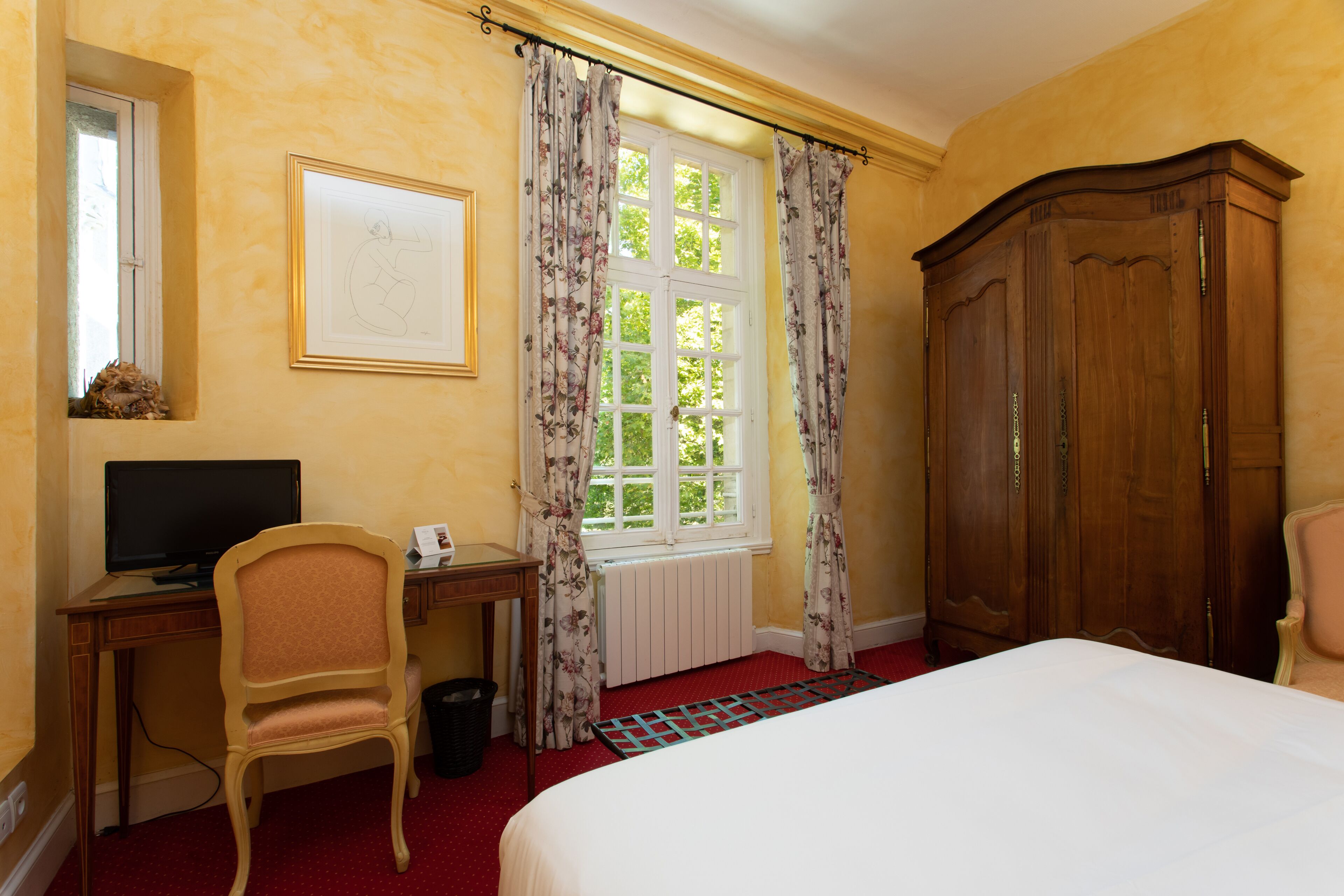 Une chambre d’hôtel comprenant un lit, un bureau avec un ordinateur, une chaise, une armoire et une fenêtre avec des rideaux.