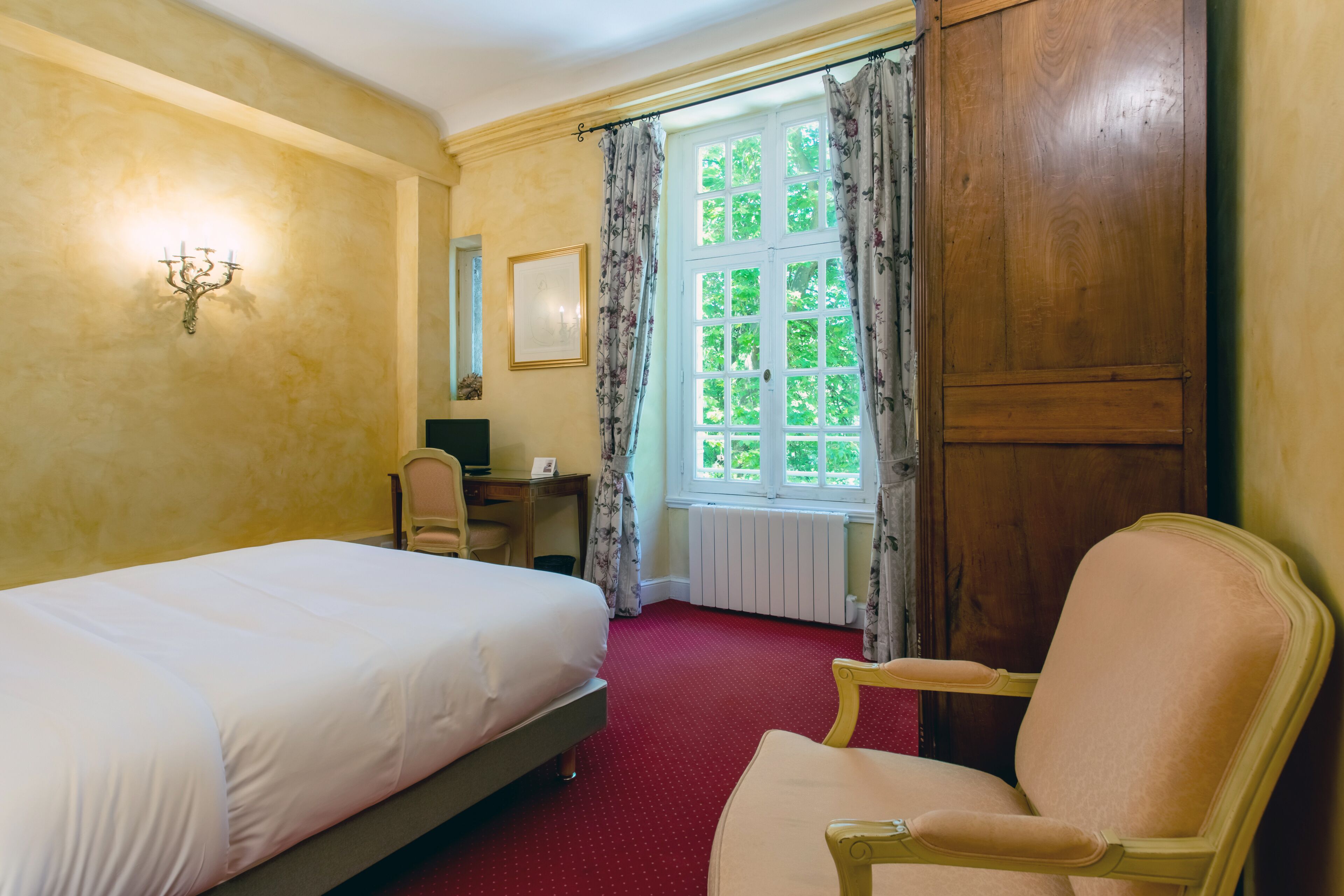 Une chambre d’hôtel avec un grand lit, une armoire en bois, un bureau avec une chaise et une fenêtre avec des rideaux.