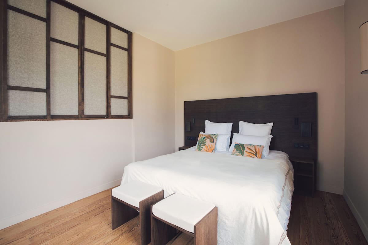 A bedroom with a large bed, wooden headboard, and a window with a view of the outside.