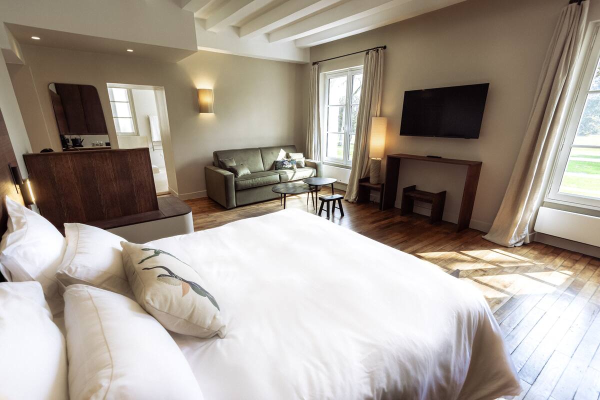 A spacious bedroom with a large bed, a sofa, a small table, a TV, and a fireplace.