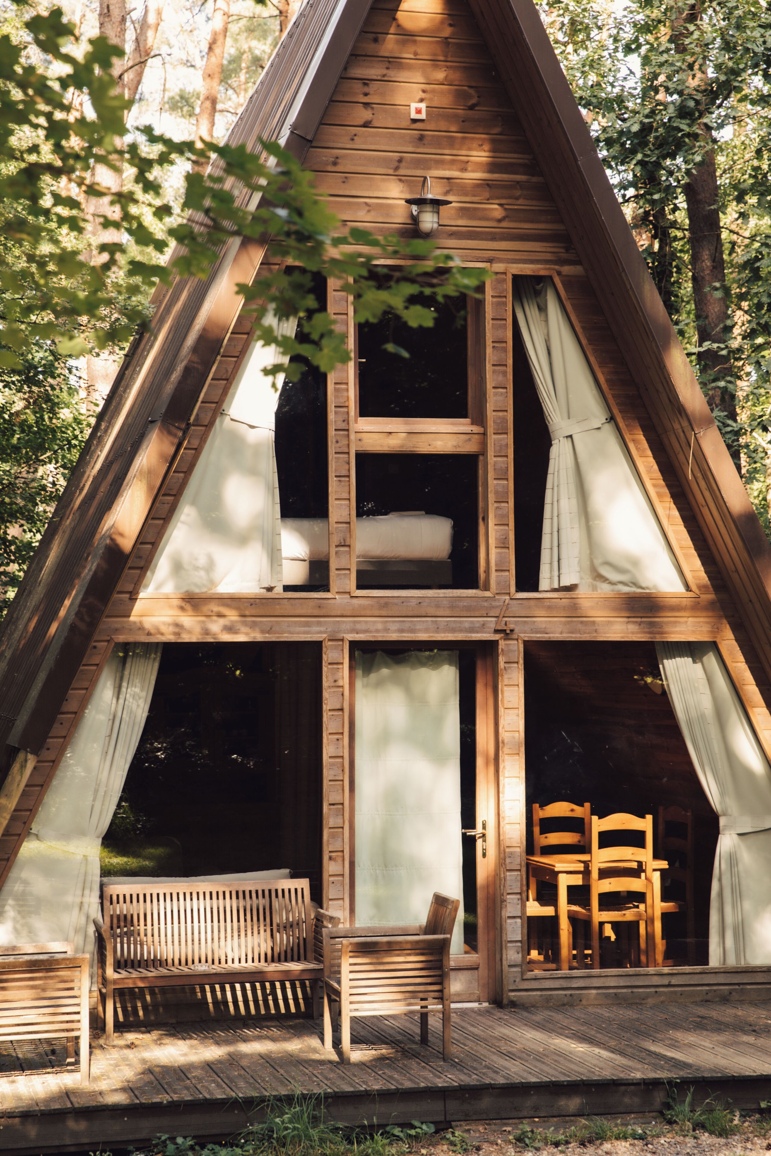Une cabane en bois avec une chambre à coucher située en mezzanine, un porche avec un banc et un coin repas avec des chaises.