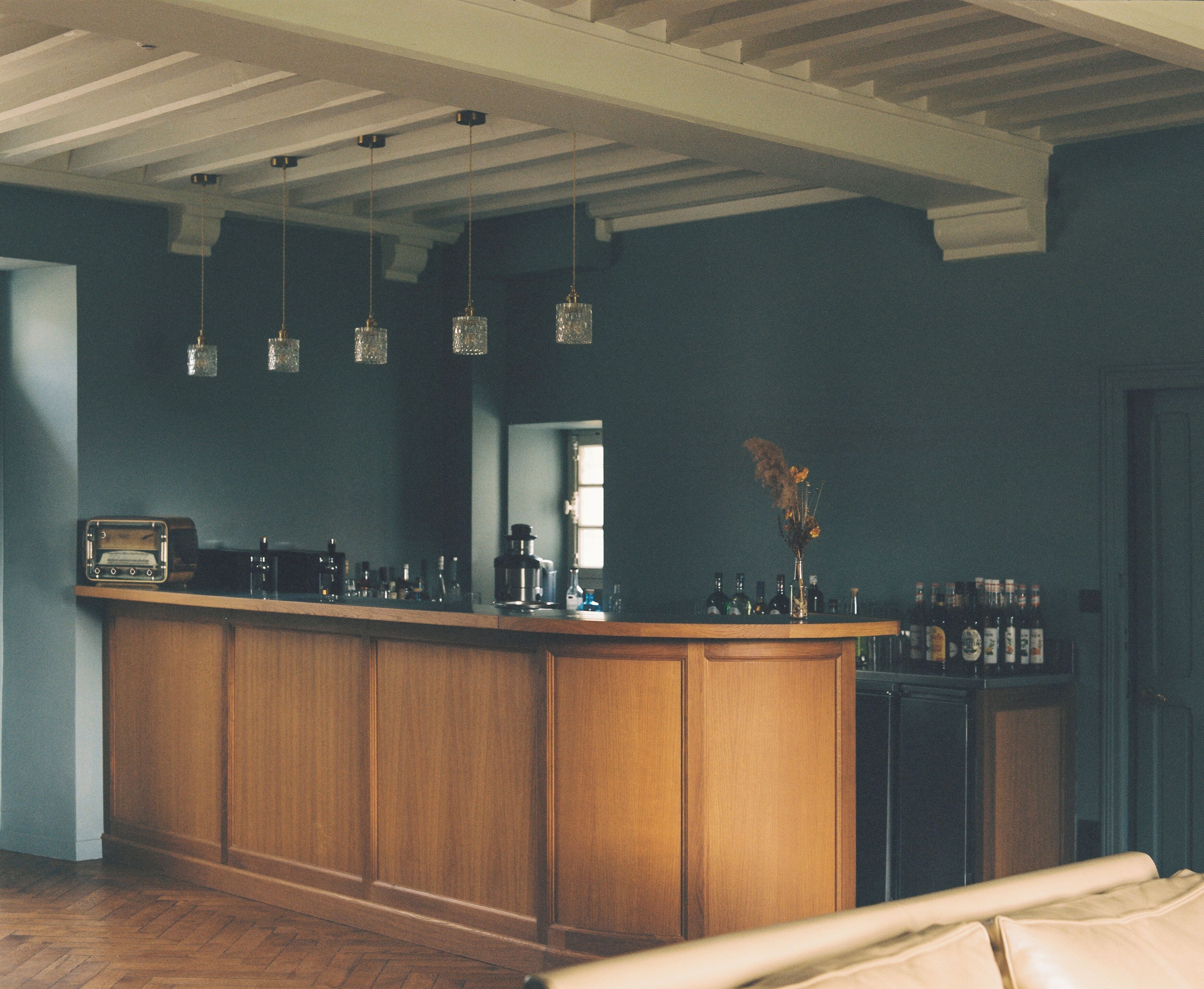 A bar area with wooden cabinets, hanging light fixtures, and a variety of bottles.