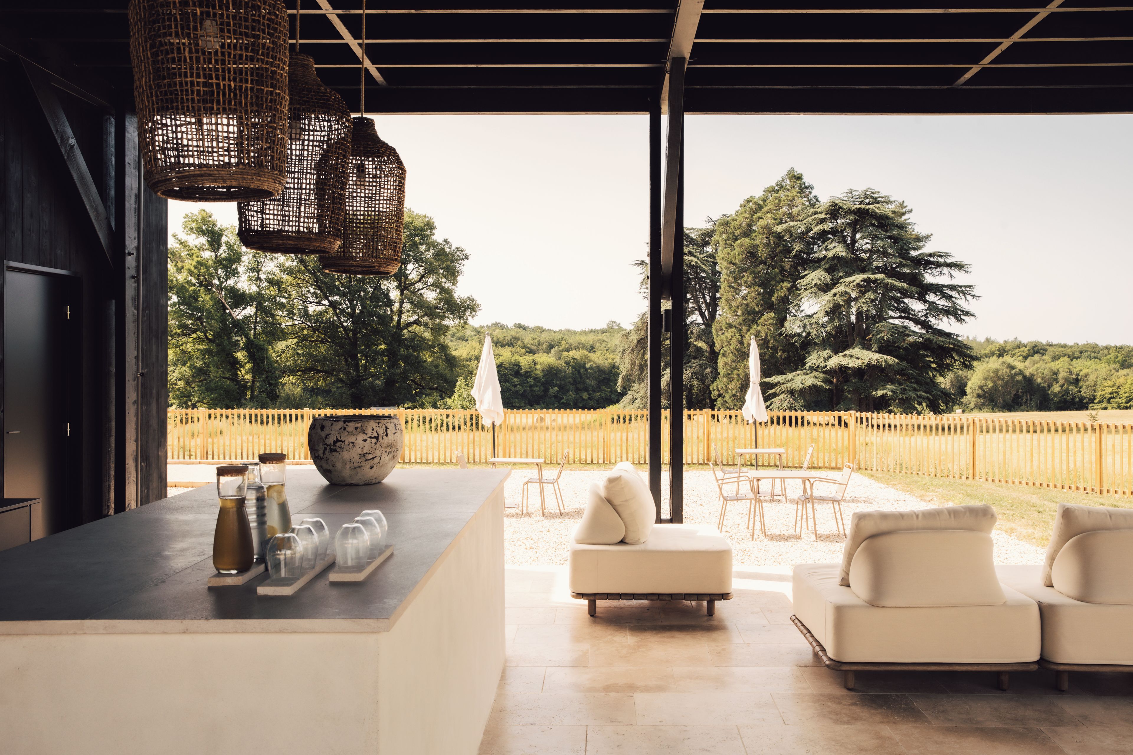 Um pátio externo com área de bar, assentos e vista para uma área arborizada.