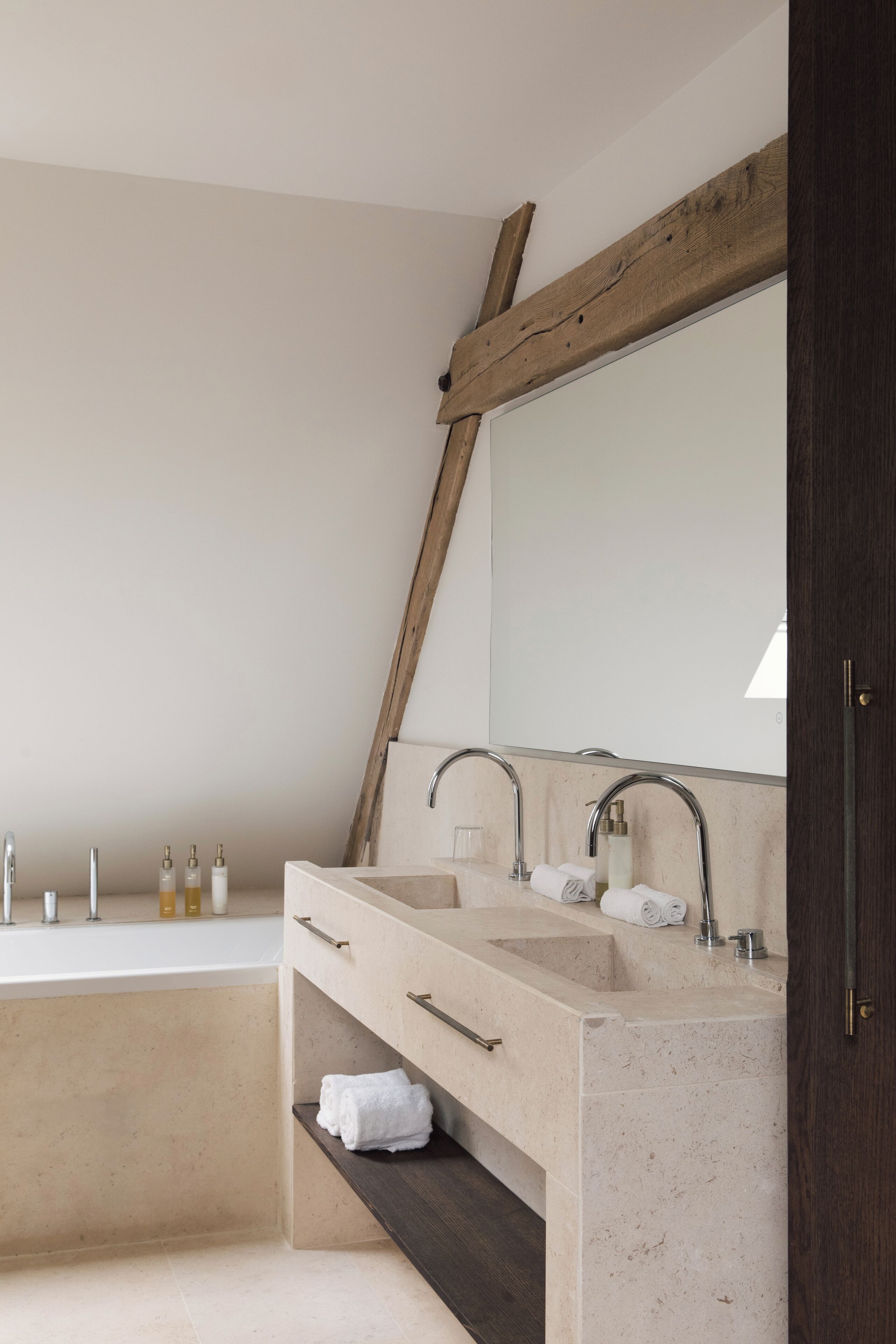 A modern bathroom with a large bathtub, two sinks, and a wooden beam ceiling.