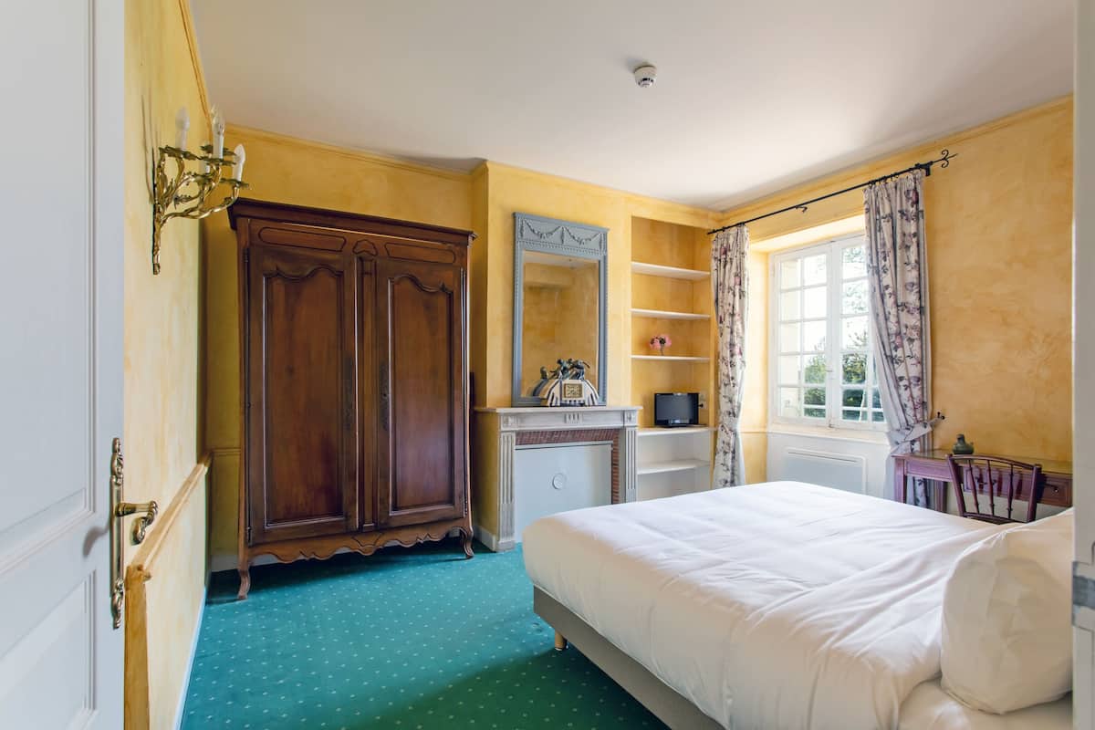 A bedroom with a large bed, a wardrobe, a dresser, a mirror, and a window with curtains.