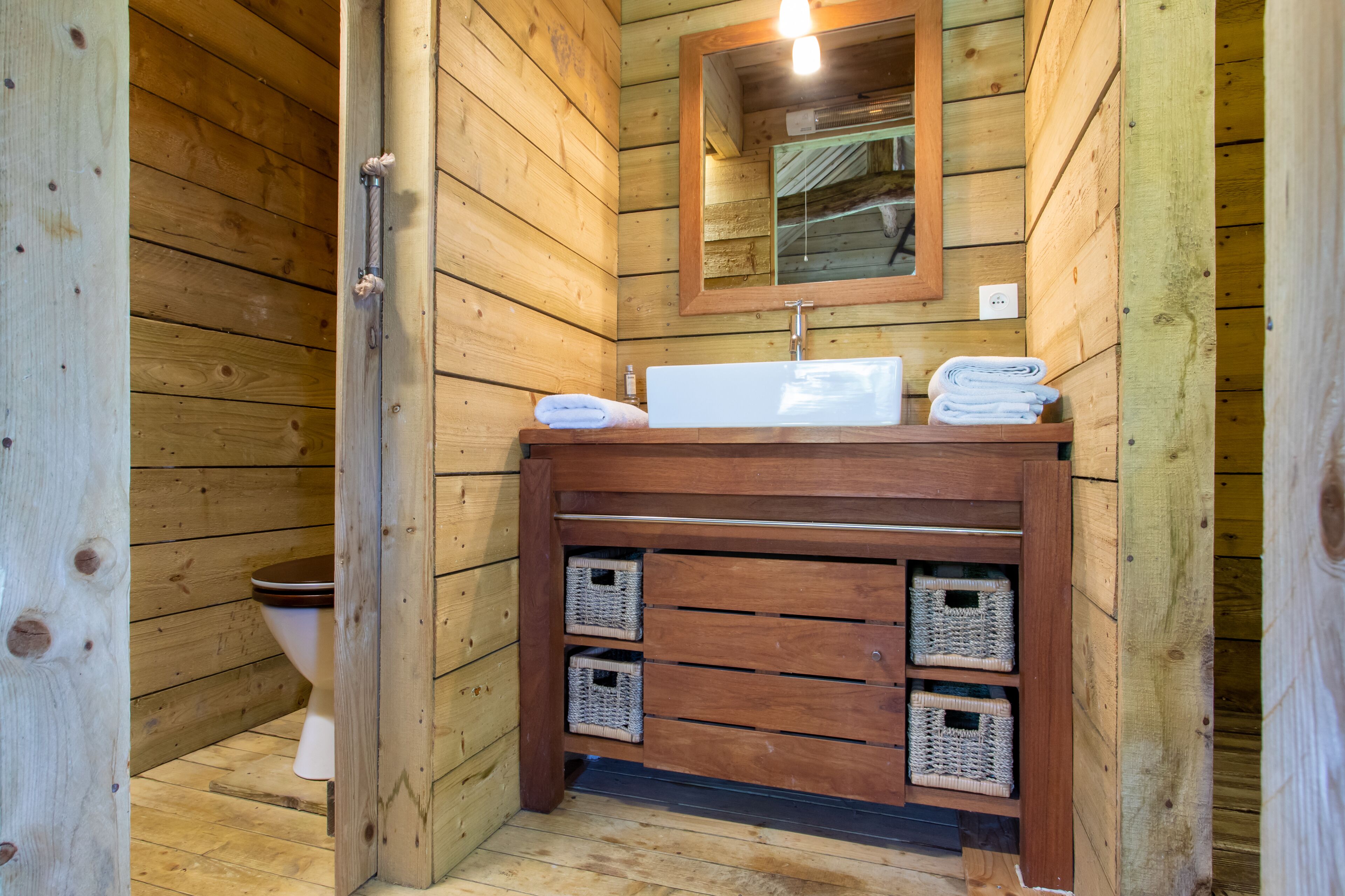 A wooden cabin bathroom with a wooden vanity, a sink, and two wicker baskets.
