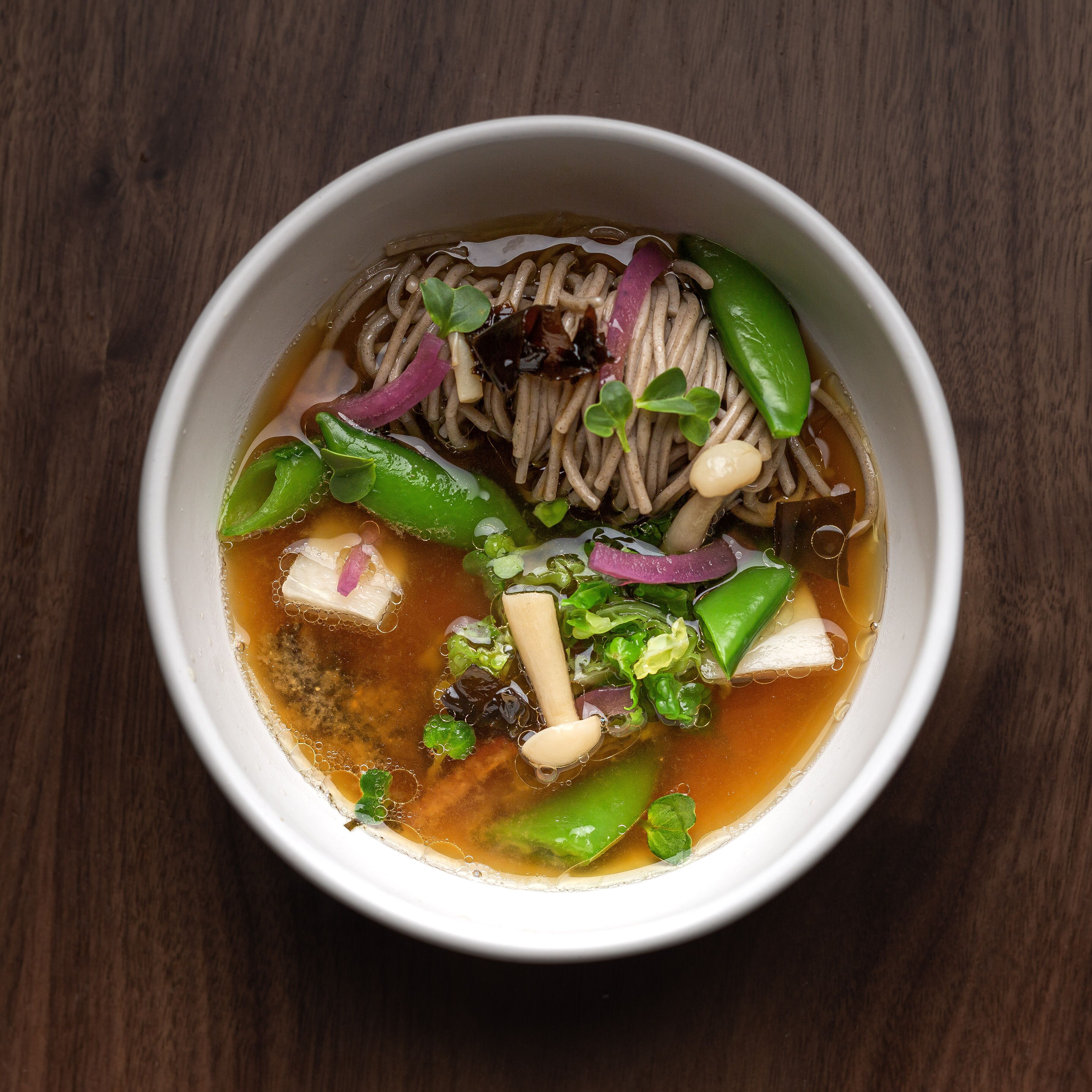 Un tazón de sopa de fideos con verduras y tofu sobre una mesa de madera.