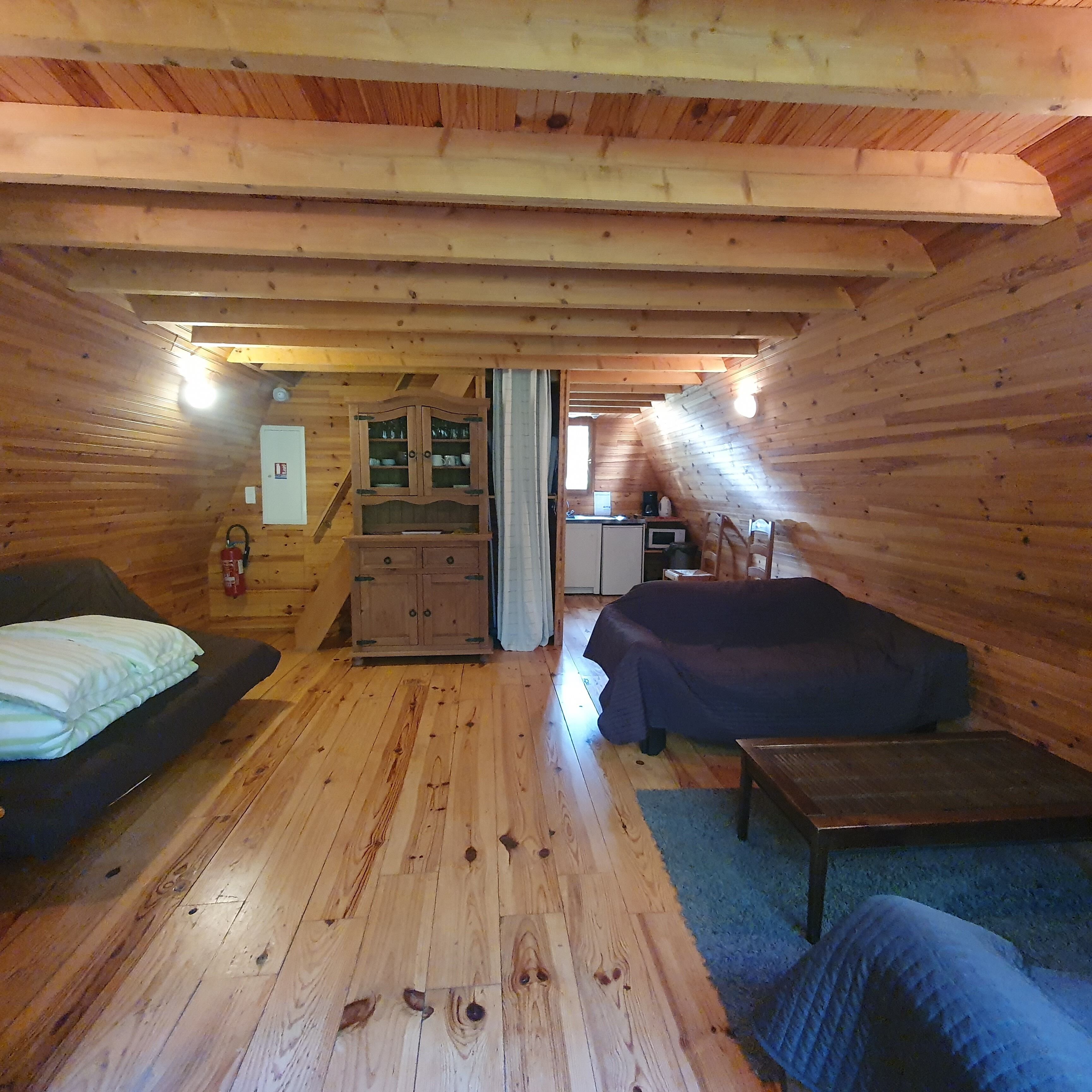 A cozy cabin with a wooden interior, a bed, a sofa, a small table, and a kitchenette.
