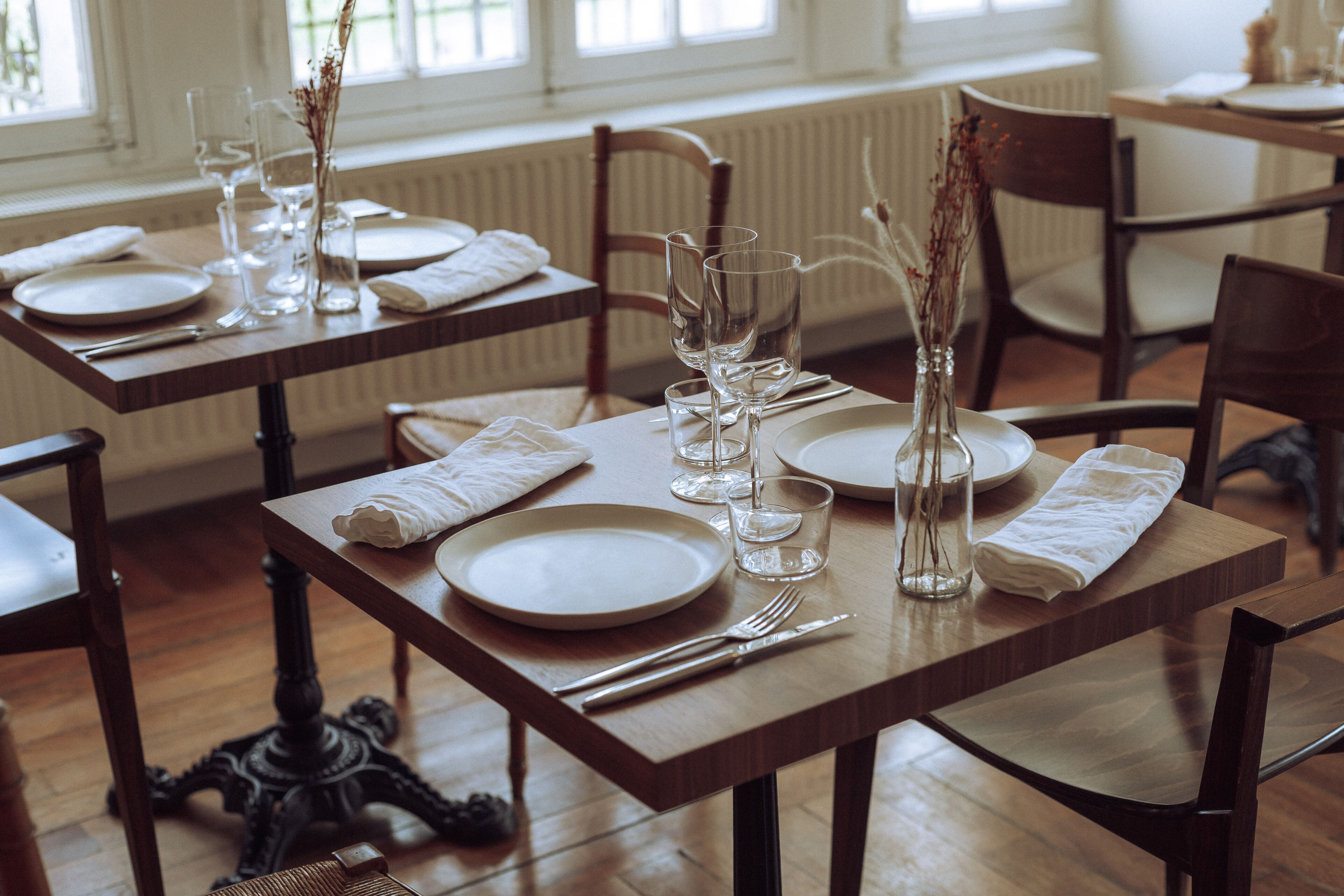 Una mesa de comedor dispuesta con platos, vasos y cubiertos, con sillas alrededor.