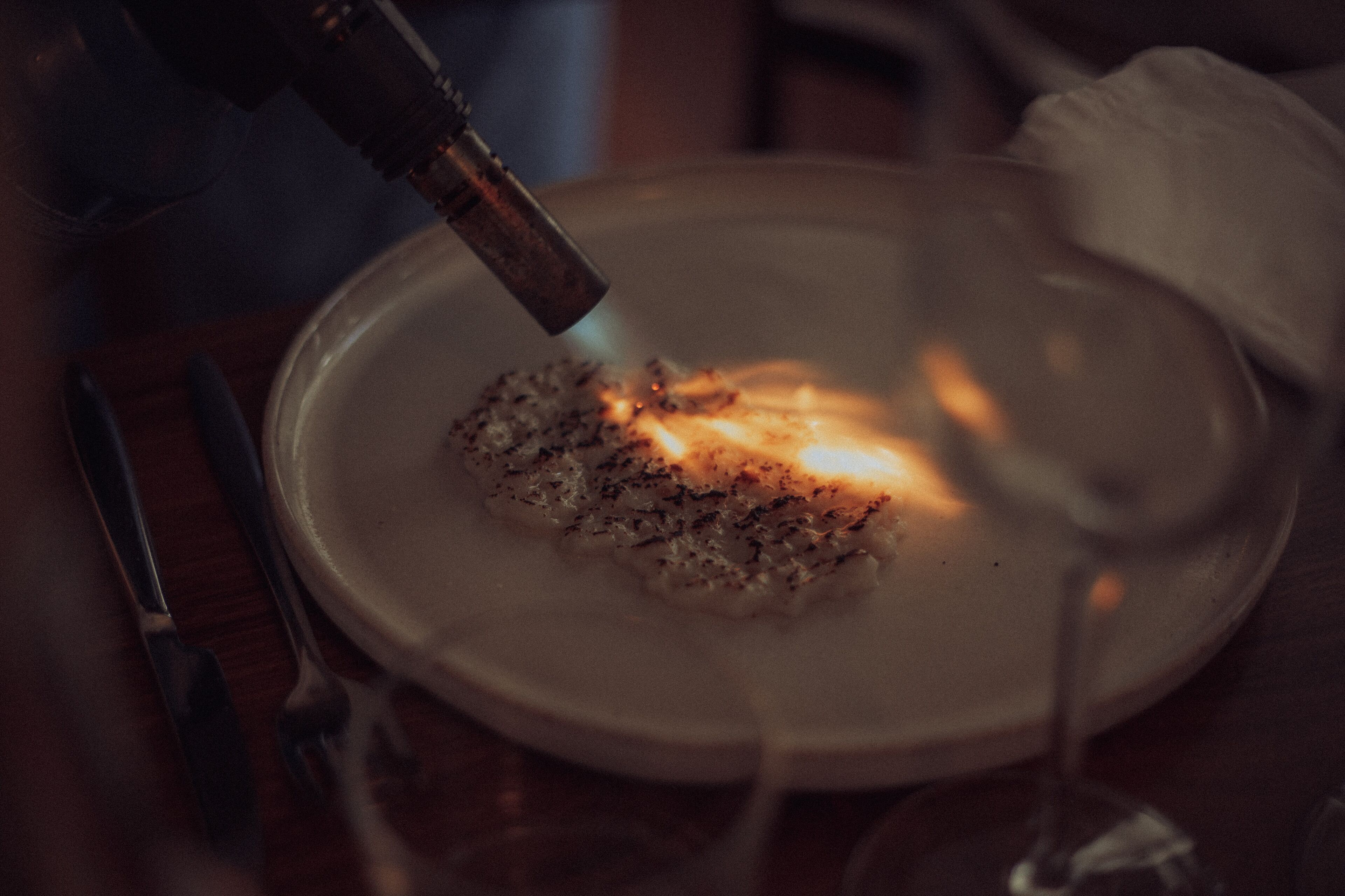 A close-up of a plate with food being toasted with a blowtorch.