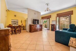 A living room with a TV, wooden furniture, a sofa, and a dining area with chairs and a table. - Grande Platano | Apartment with Patio 5 min from Sorrento (Piano di Sorrento)