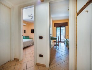 Un pasillo que conduce a un dormitorio con cama, un comedor con mesa y sillas, y una cocina con mostrador y armarios.