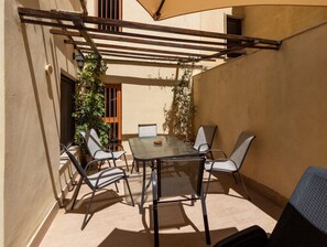 Um pátio externo com mesa e cadeiras, uma pérgula e um vaso de planta.