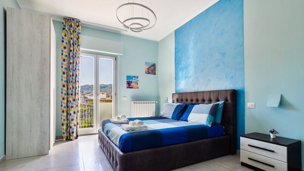 A bedroom with a large bed, a nightstand, a view through a sliding door, and a ceiling light fixture.