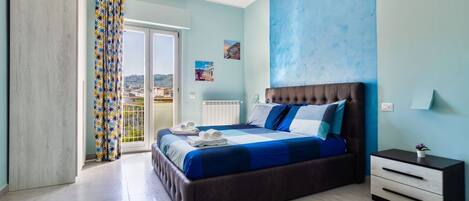 A bedroom with a large bed, a nightstand, a view through a sliding door, and a ceiling light fixture.