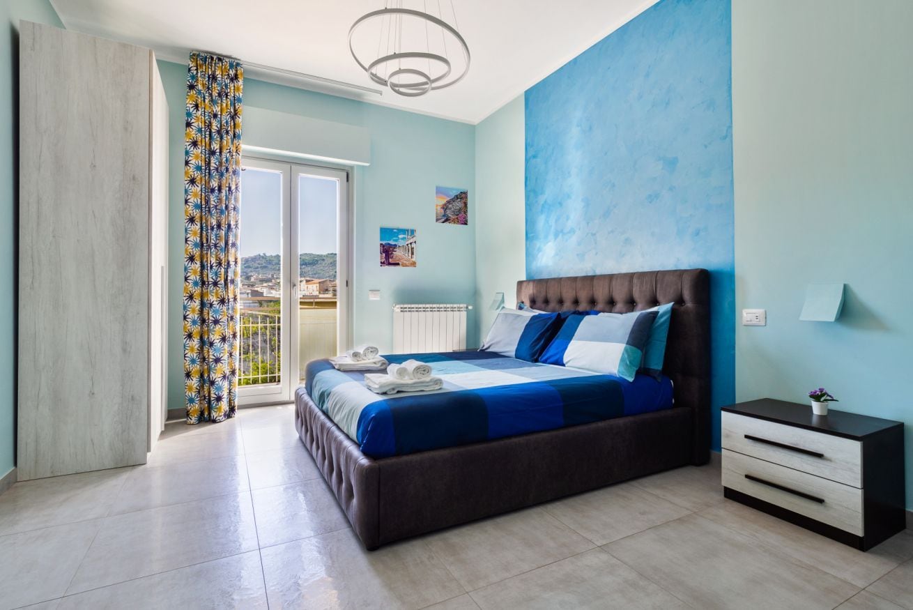 Un dormitorio con una cama grande, una mesita de noche, vista a través de una puerta corrediza y una lámpara en el techo.