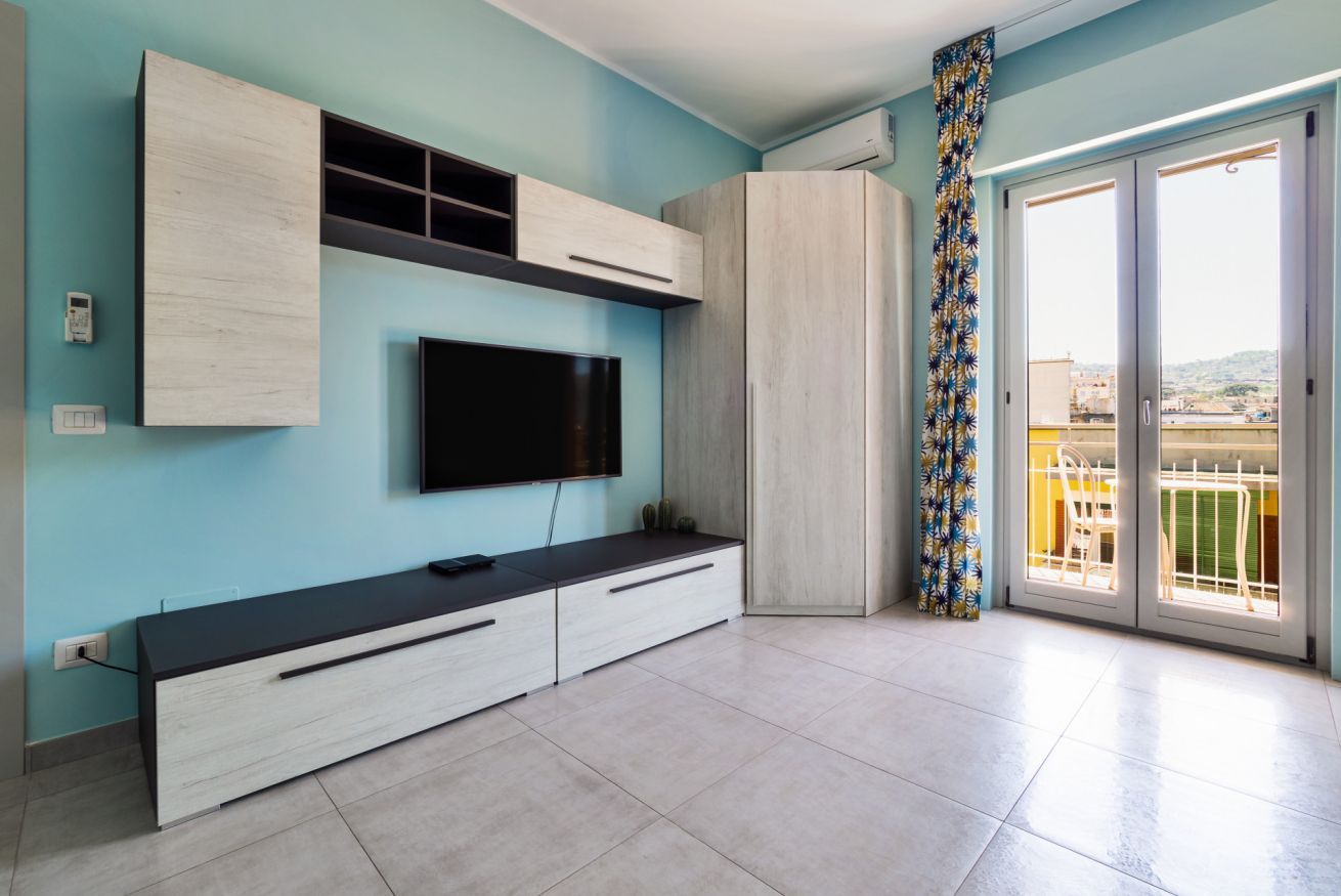 Uma sala de estar moderna com televisão de tela plana, armários embutidos e uma varanda com cortina estampada.