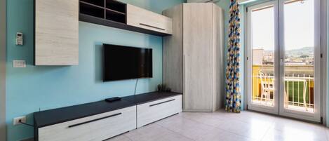 A modern living room with a flat-screen TV, built-in cabinets, and a balcony with a patterned curtain.