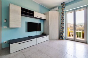 Un salon moderne doté d’un téléviseur à écran plat, de placards intégrés et d’un balcon agrémenté d’un rideau à motifs.