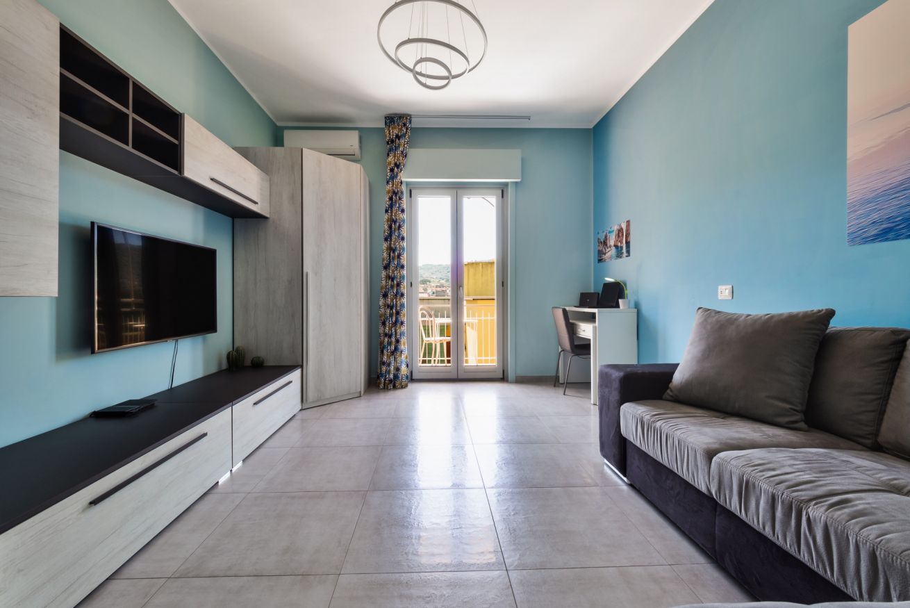 Una sala de estar moderna con un televisor de pantalla plana, un sofá, un comedor y vistas a través de una puerta de cristal.