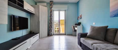 Una sala de estar moderna con un televisor de pantalla plana, un sofá, un comedor y vistas a través de una puerta de cristal.