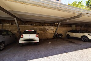 Un estacionamiento con tres coches aparcados bajo una zona techada.