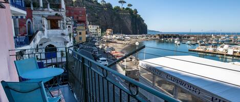 A balcony with a view of a marina, a restaurant named 'Ristorante Capprodo PIZZA,' and buildings along the coastline.