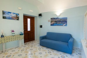 A room with a blue sofa, a wooden door, a tiled floor with a floral pattern, a small table with a vase and figurines, and two wall-mounted pictures. - Casa Mariarosa - Seaview House in Sorrento Coast (Piano di Sorrento)