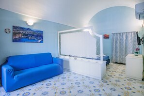 Una habitación con un sofá azul, un armario blanco, un ventanal con cortina y un cuadro colgado en la pared.