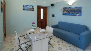A dining area with a table set for two, a blue sofa, and a door leading to another room. - Casa Mariarosa - Seaview House in Sorrento Coast (Piano di Sorrento)