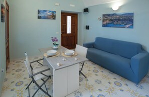 A dining area with a table set for two, a blue sofa, and a door leading to another room.