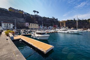 A marina with boats docked, a wooden dock, and buildings on a cliff.