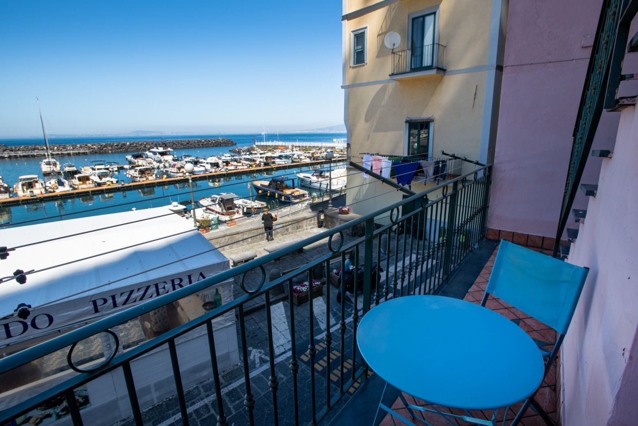 A balcony with a view of a marina, a table, and chairs.
