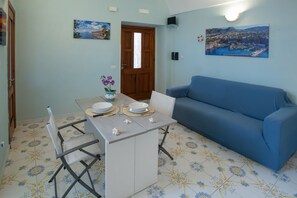 A dining area with a table set for two, a blue sofa, and a door leading to another room. - Casa Mariarosa - Seaview House in Sorrento Coast (Piano di Sorrento)