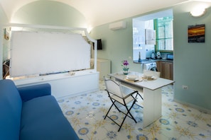 A compact living space with a sofa, a small dining table, and a kitchen area. - Casa Mariarosa - Seaview House in Sorrento Coast (Piano di Sorrento)