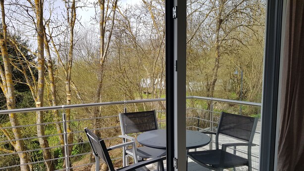 A balcony with a table and chairs, overlooking a forested area.