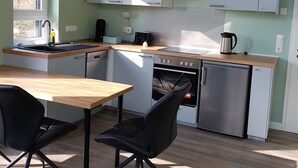 A modern kitchen with light green walls, a wooden countertop, and stainless steel appliances. There is a dining table with two chairs.