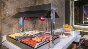 Ein Buffet mit verschiedenen Speisen, eine Holbschüssel mit Früchten und ein Fenster im Hintergrund.