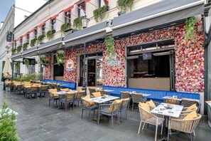 An outdoor cafe with wicker tables and chairs, a blue bench, and a floral wall decoration. - Hotel Forty One Bucharest (Bucharest)