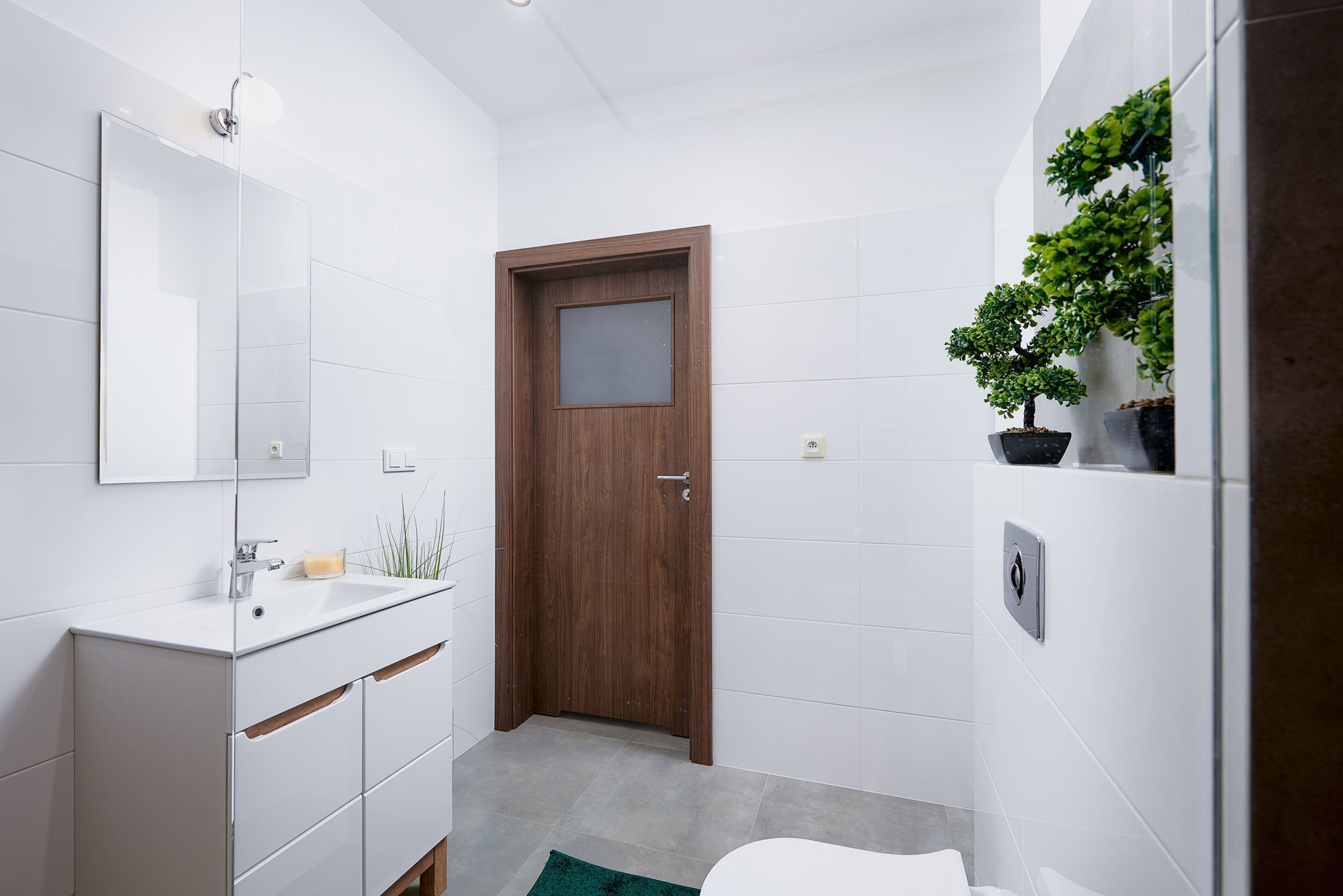 A modern bathroom with a white vanity, a wooden door, and a potted plant.