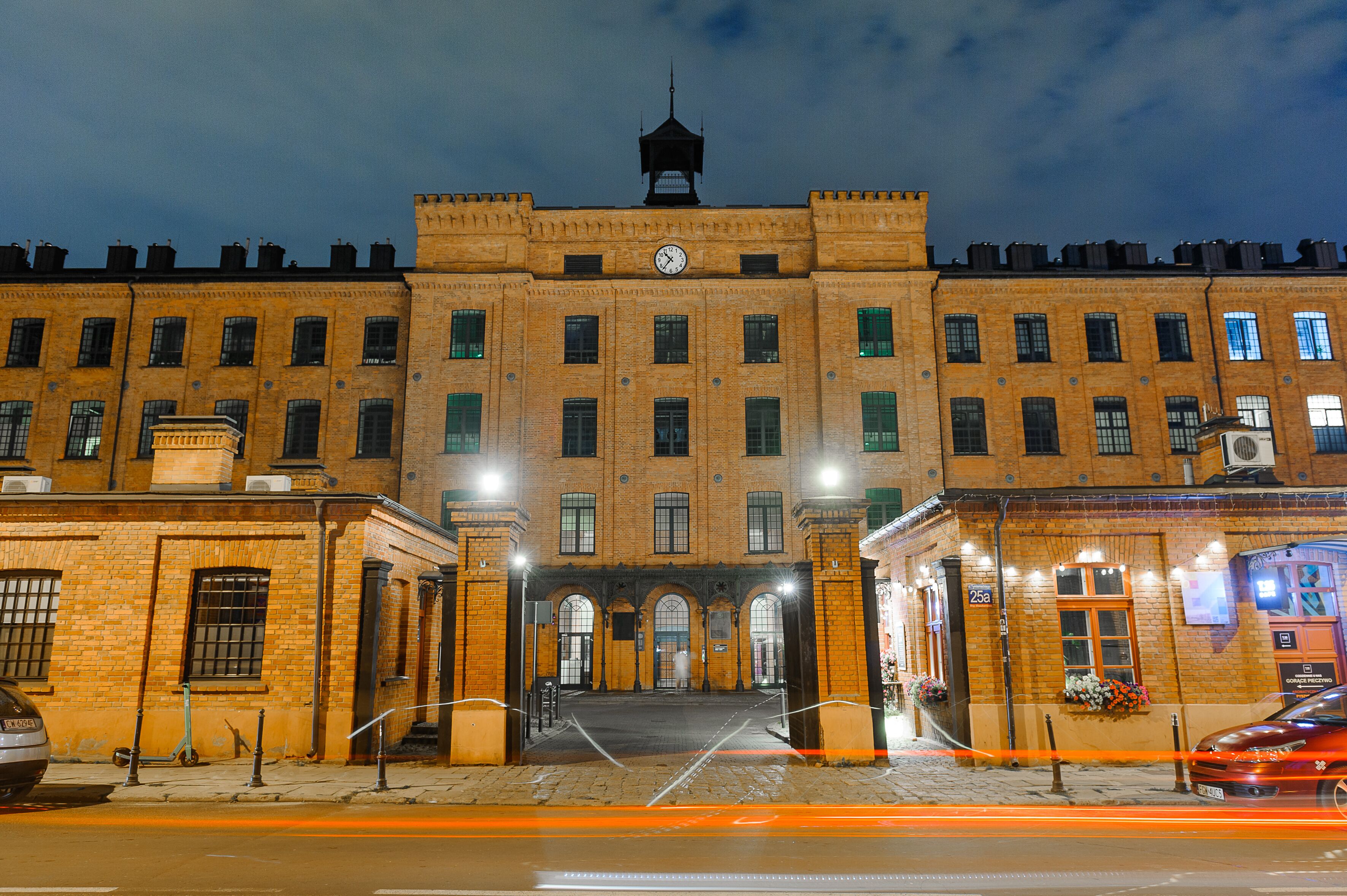 A large, historic building with a central clock tower, arched entrance, and multiple windows.