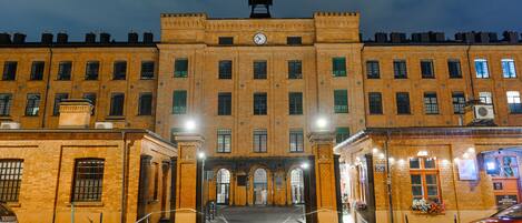 A large, historic building with a central clock tower, arched entrance, and multiple windows.