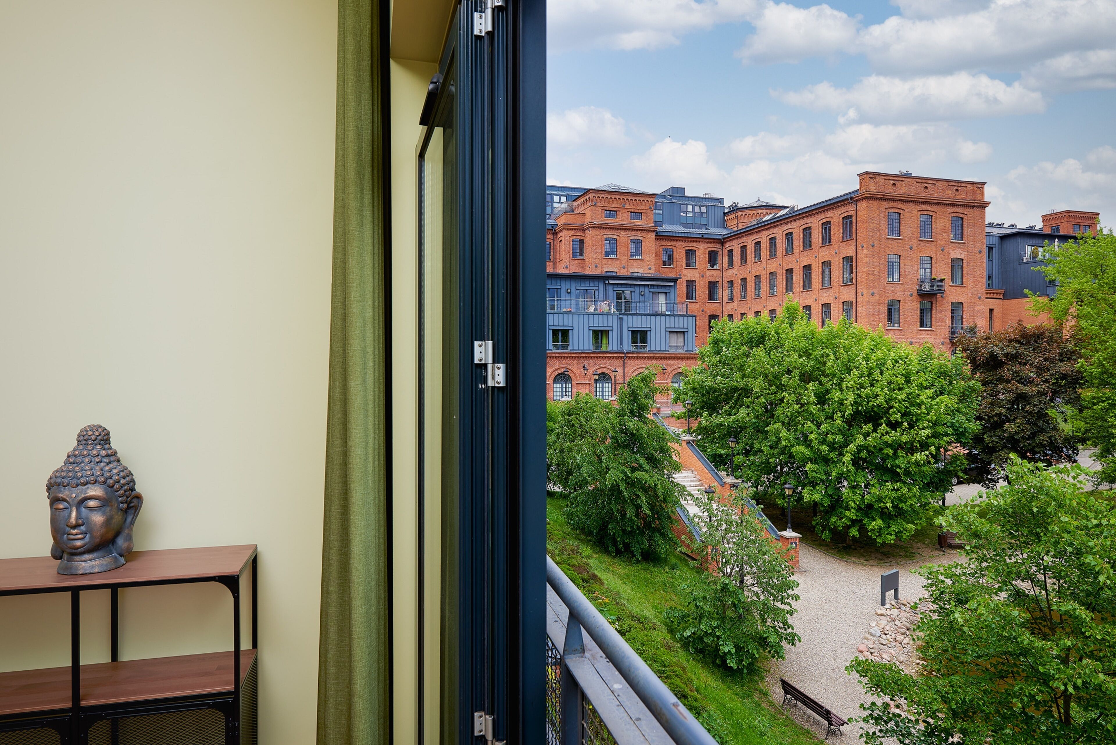 En utsikt från en balkong med utsikt över en innergård med en Buddha-staty, en träbänk och en byggnad med röda och blå fasader.
